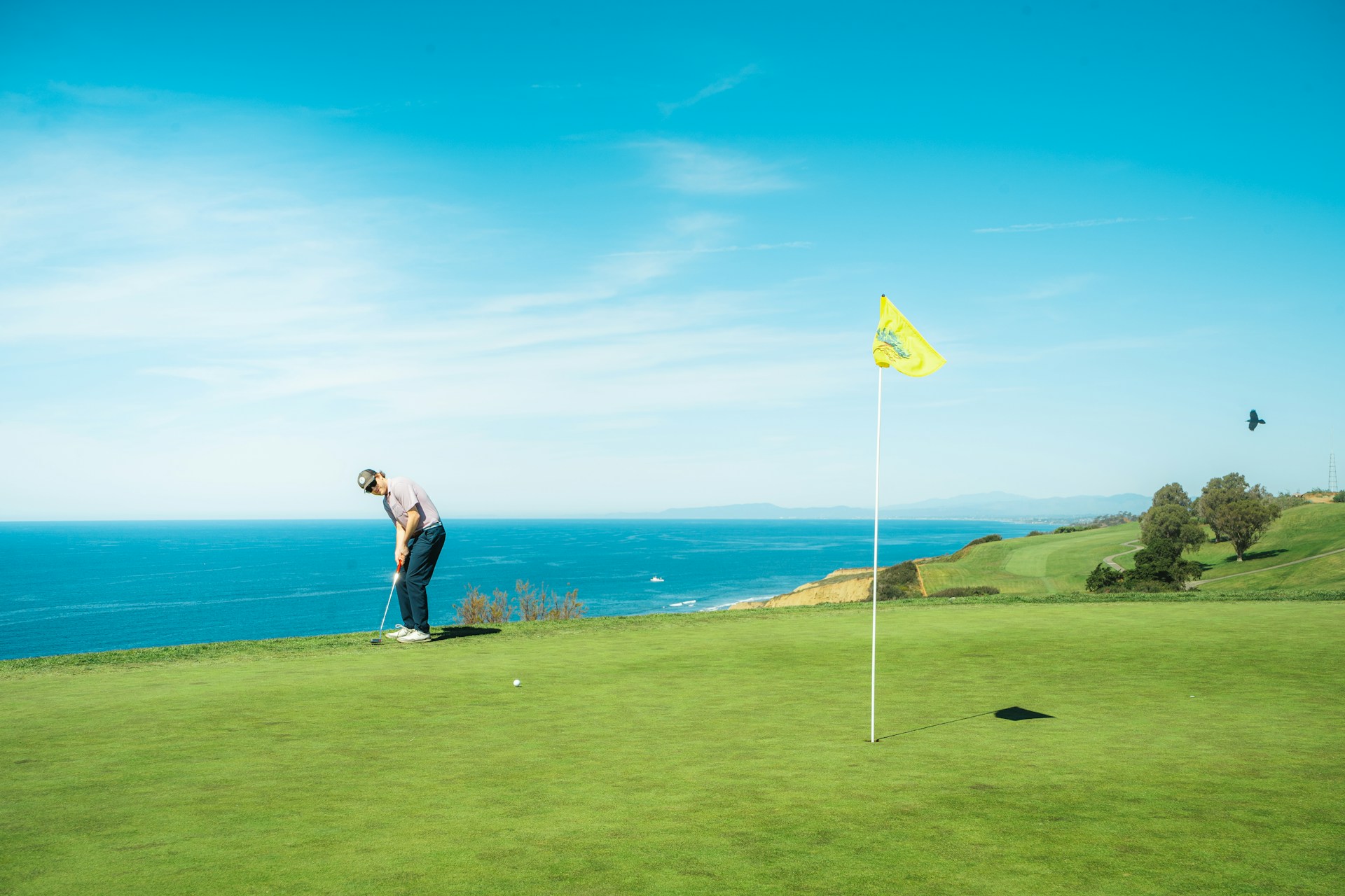 Golfer putting on a coastal golf course with sea view and yellow flag